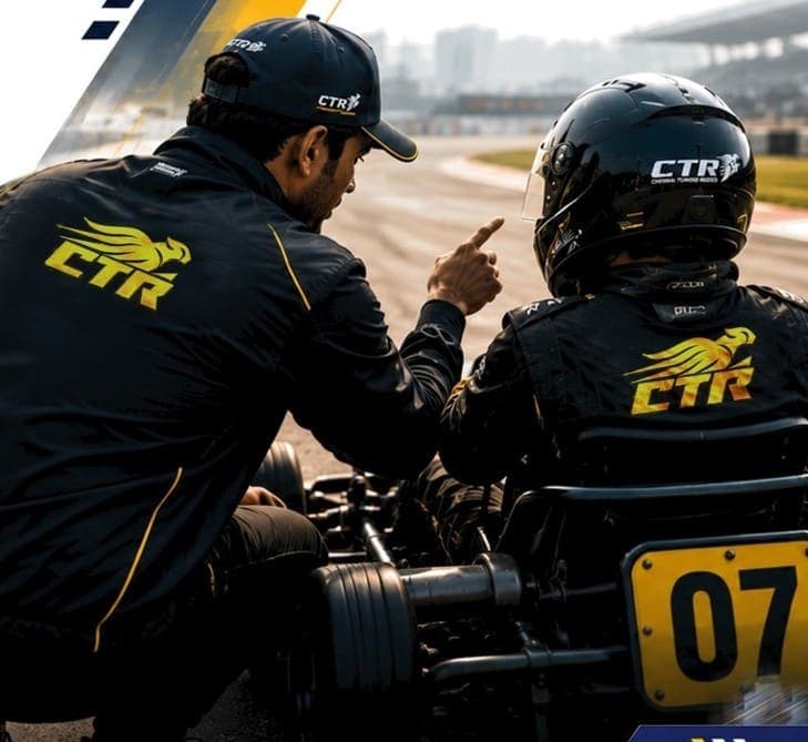 CTR coach kneeling beside a seated kart driver on track, pointing ahead.
